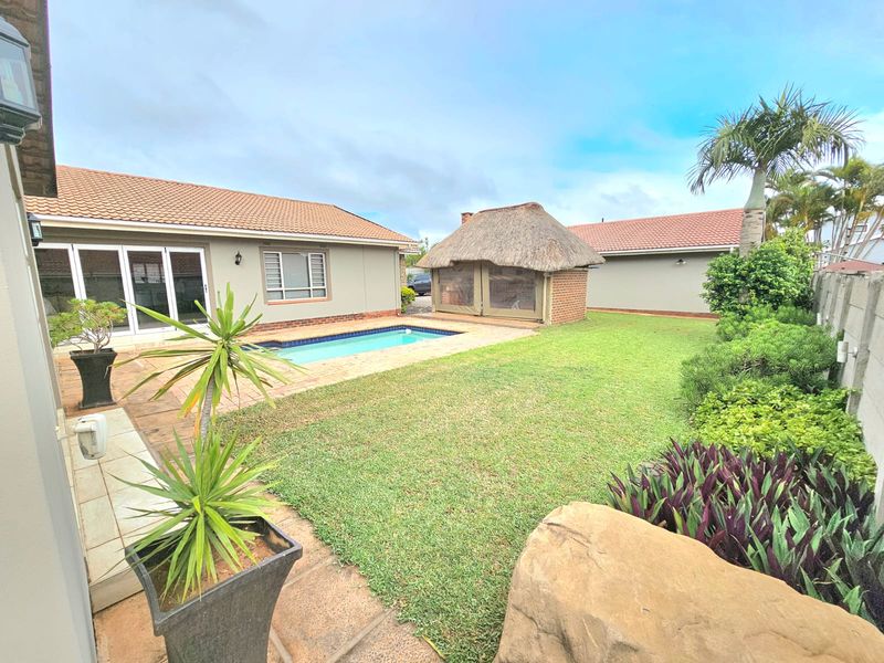 Spacious rear garden featuring a swimming pool, paved patio area, and a traditional thatched lapa structure, perfect for outdoor entertaining.