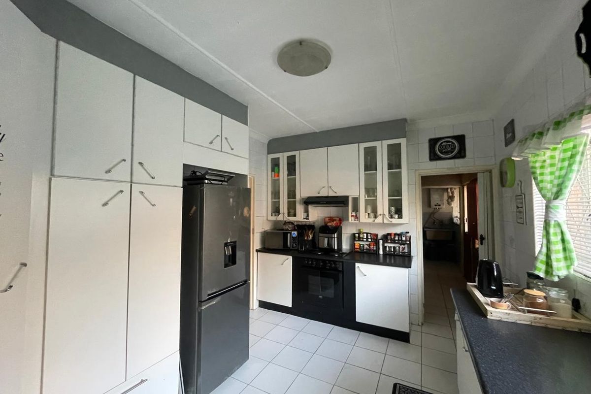 A functional kitchen featuring white and black cabinetry, built-in oven, extractor fan, and tiled flooring, with an adjacent scullery area visible.