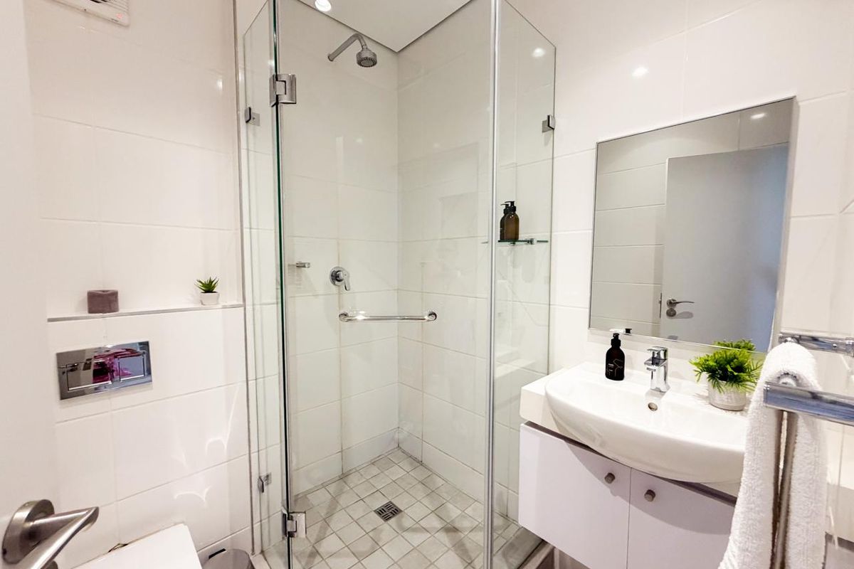 Modern bathroom featuring a glass-enclosed corner shower, wall-mounted toilet with concealed cistern, and a vanity basin with integrated storage.
