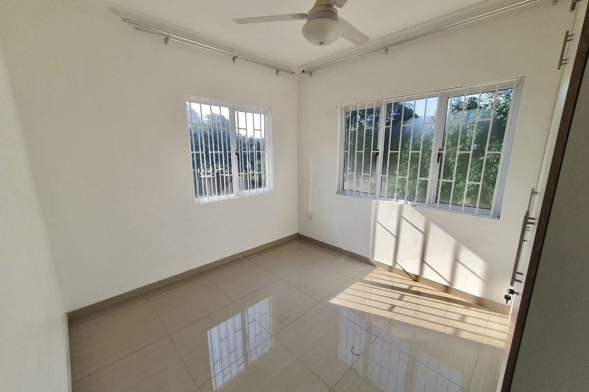 A bright, empty bedroom featuring tiled flooring, a ceiling fan, and windows fitted with security bars.