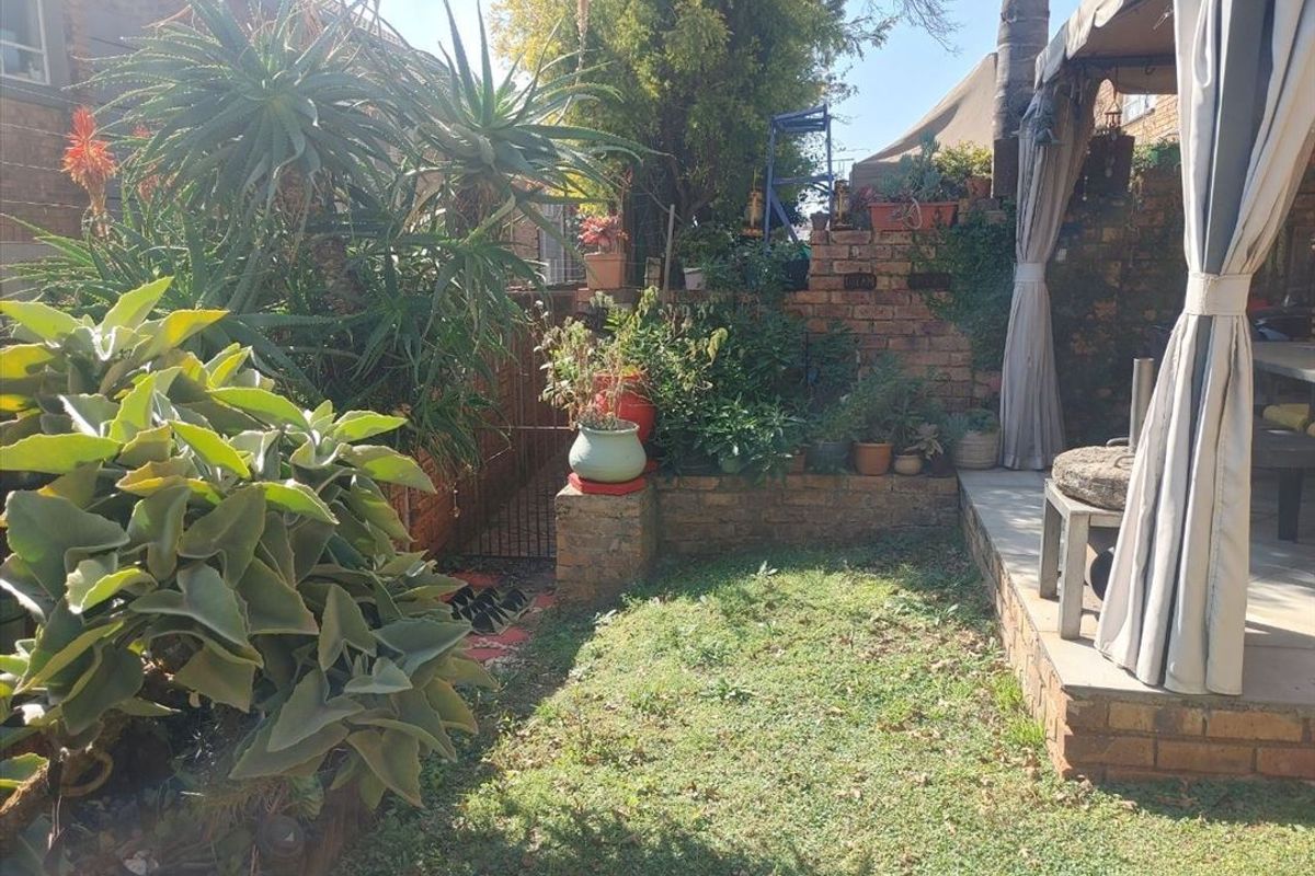A private rear garden featuring a brick retaining wall, established greenery, and a covered patio area with a paved base.