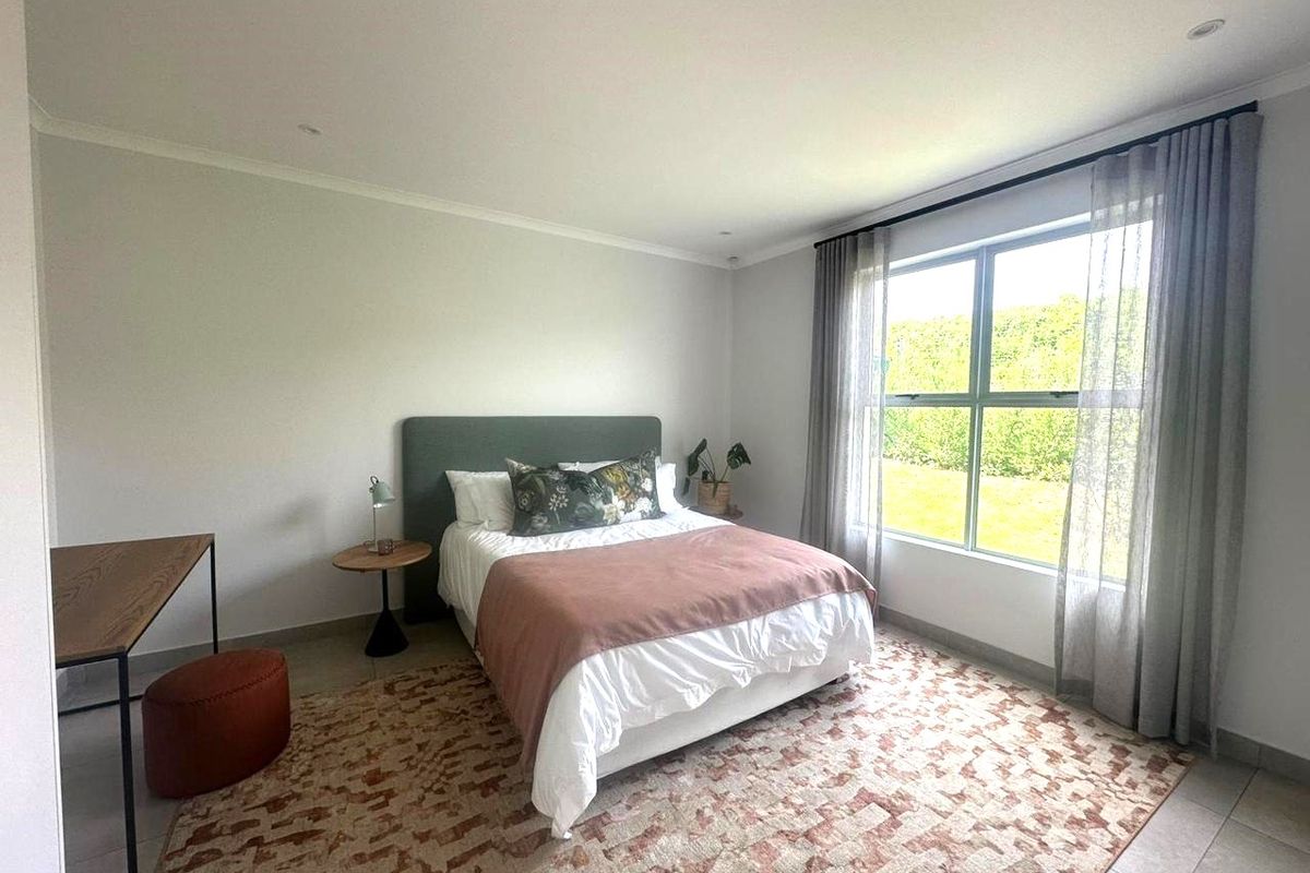 A bright and well-maintained bedroom featuring neutral walls, tiled flooring, and a large window providing natural light and garden views.