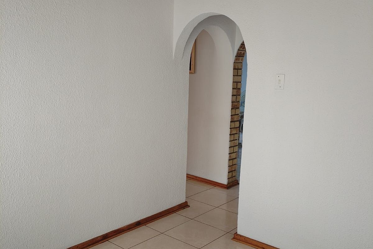 An empty interior space featuring tiled flooring, a timber-clad ceiling, and a distinctive arched doorway leading to an adjacent room.
