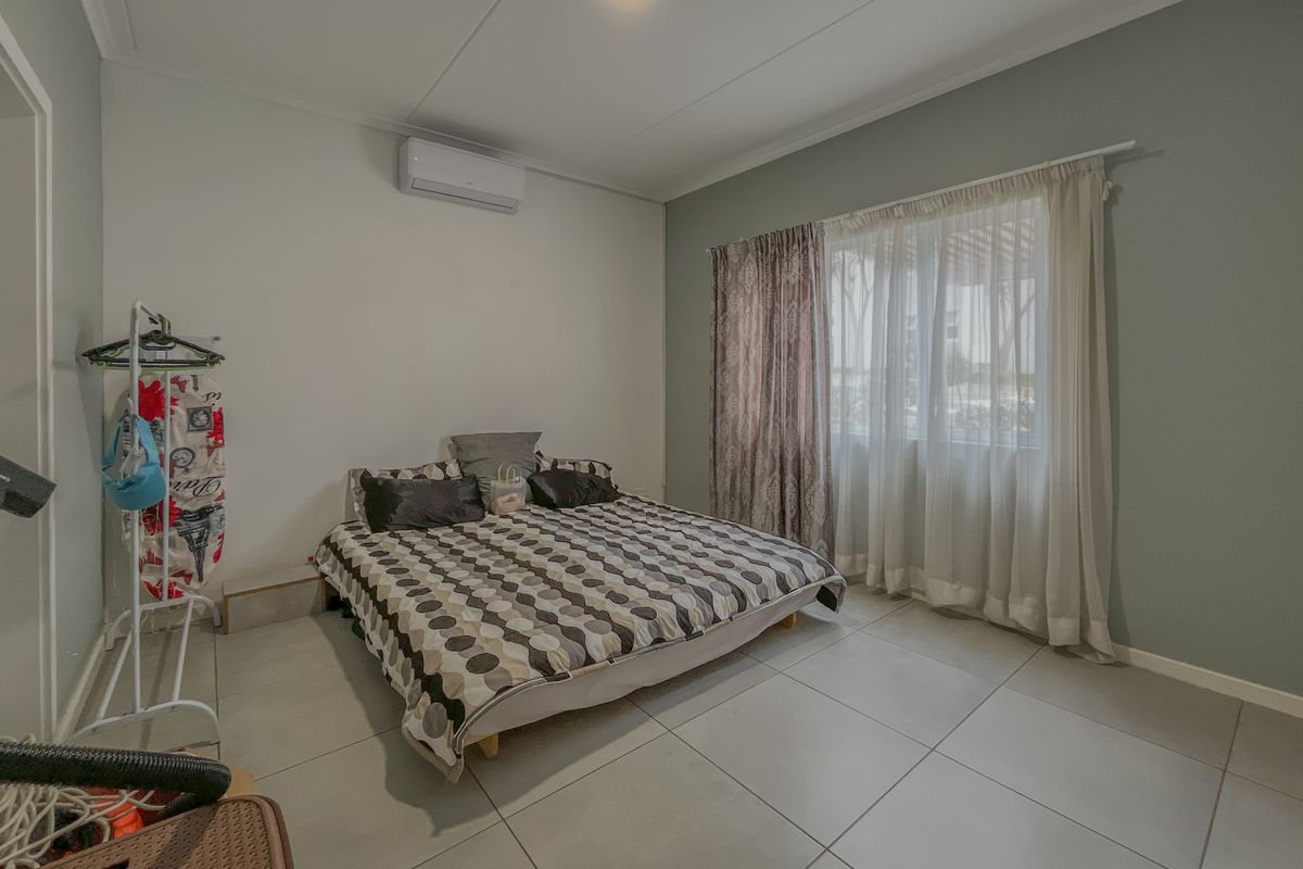 A bedroom featuring large floor tiles, a wall-mounted air conditioning unit, and a window with curtain tracks.