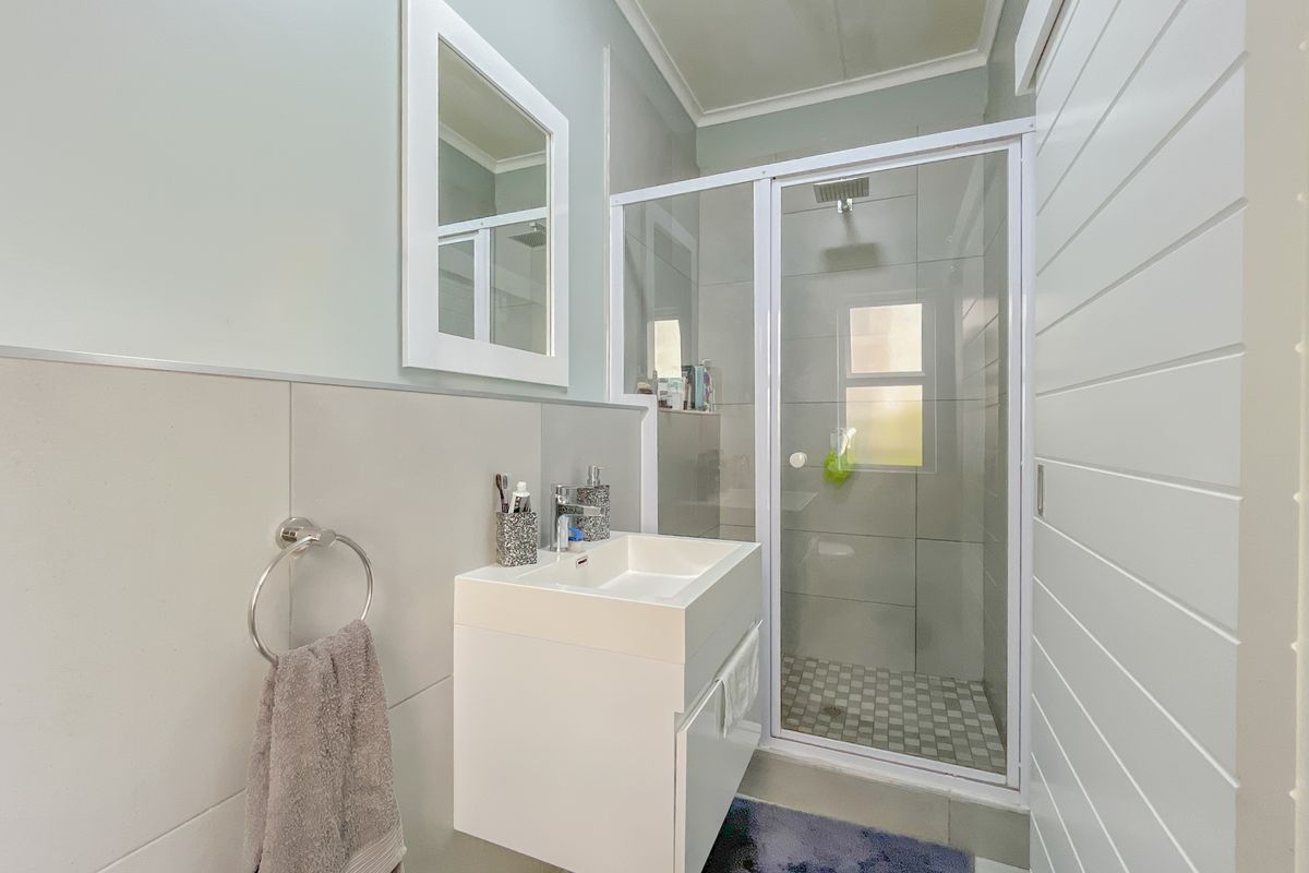 Modern bathroom featuring a wall-mounted vanity, a glass-enclosed shower with tiled flooring, and a framed mirror.