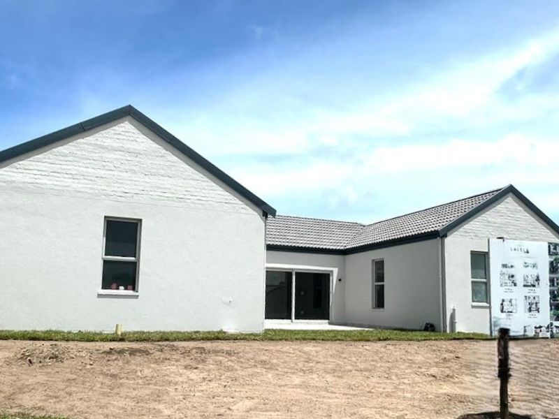 Rear view of a modern single-story house featuring a tiled roof, white painted brick exterior, and a concrete patio area with sliding glass doors.