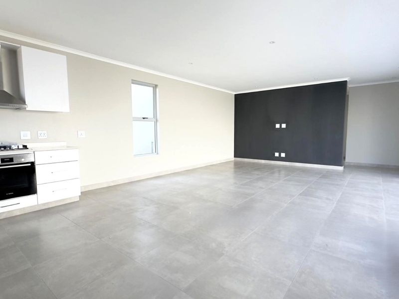 Spacious open-plan living area featuring a modern kitchen with built-in oven, gas hob, extractor fan, and large format floor tiles.