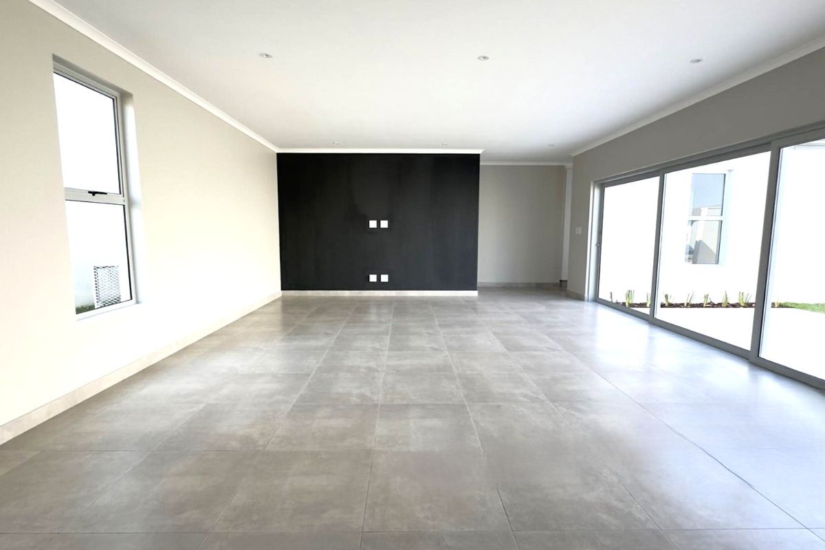 A spacious, modern, and empty living area featuring large format floor tiles, a striking black feature wall, and expansive sliding glass doors to the garden.