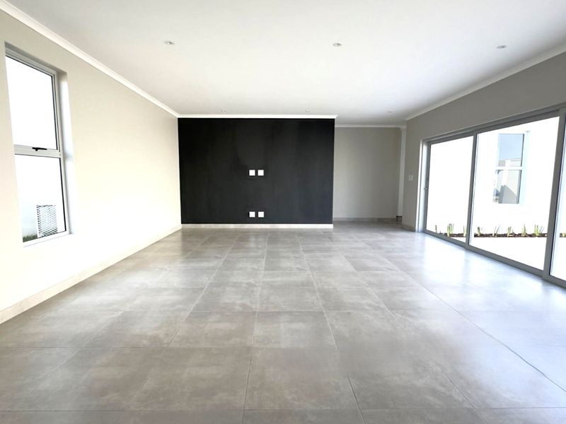 A spacious, modern, and empty living area featuring large format floor tiles, a striking black feature wall, and expansive sliding glass doors to the garden.