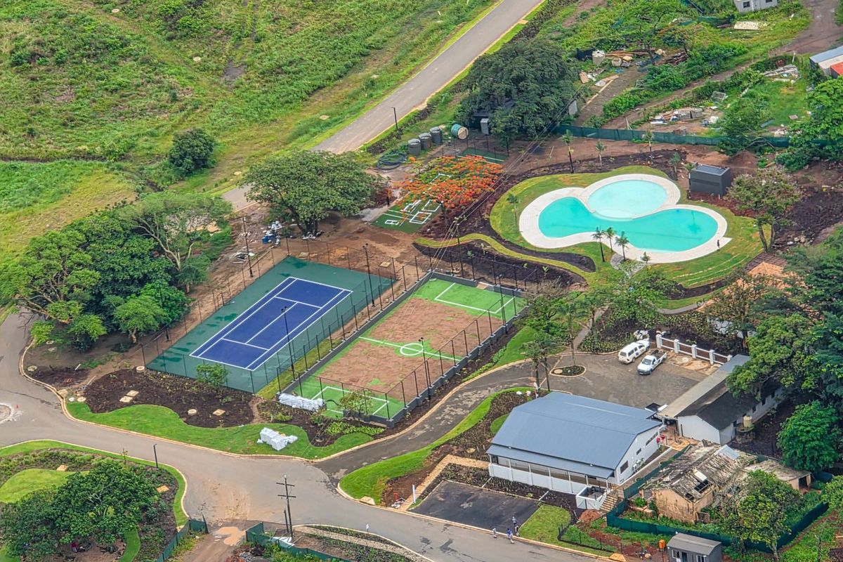 Aerial view of a recreational facility featuring a tennis court, multi-purpose sports court, swimming pool, and surrounding landscaped grounds.