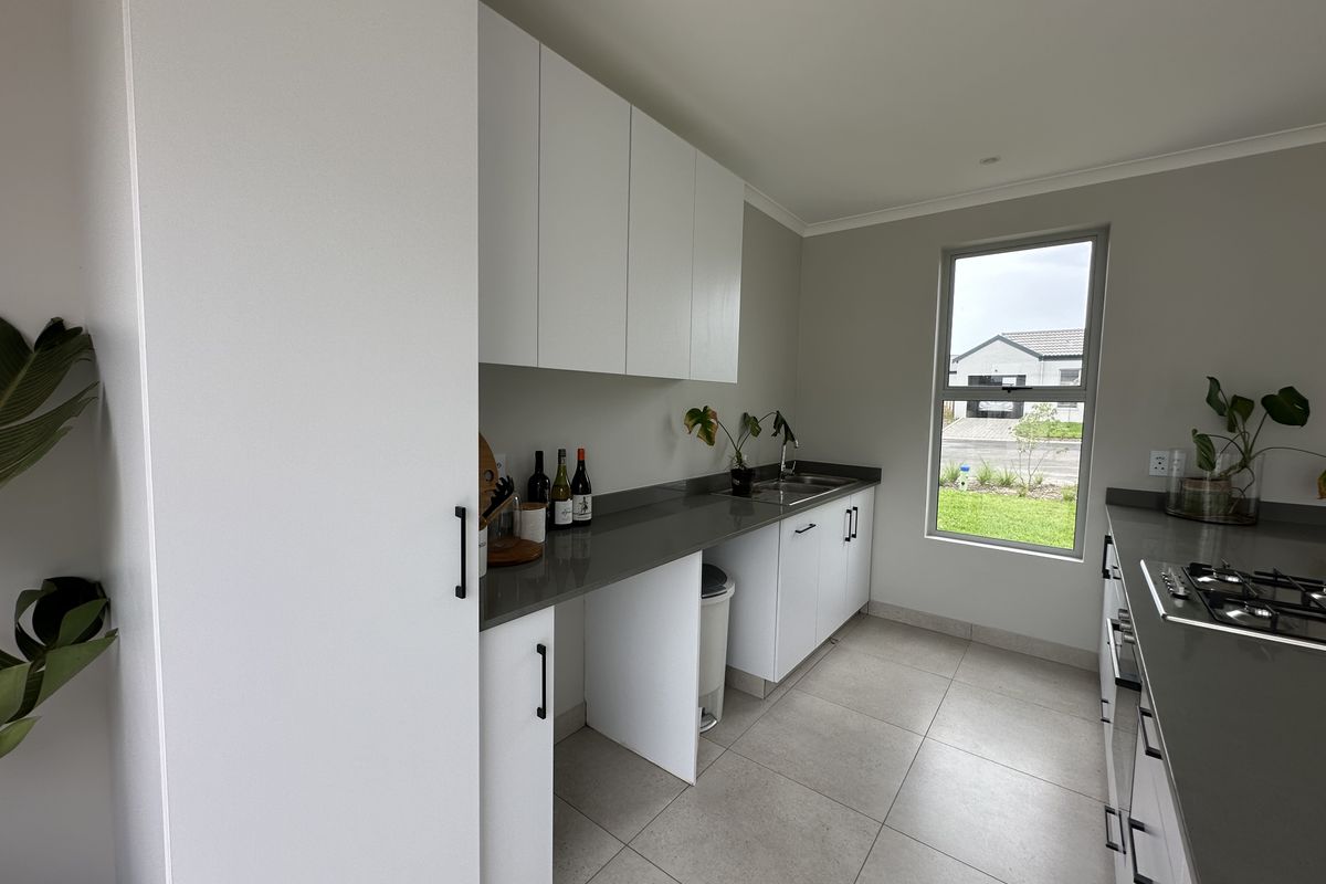 Modern kitchen featuring sleek white cabinetry, dark stone countertops, a built-in gas hob, and tiled flooring with a view of the exterior.