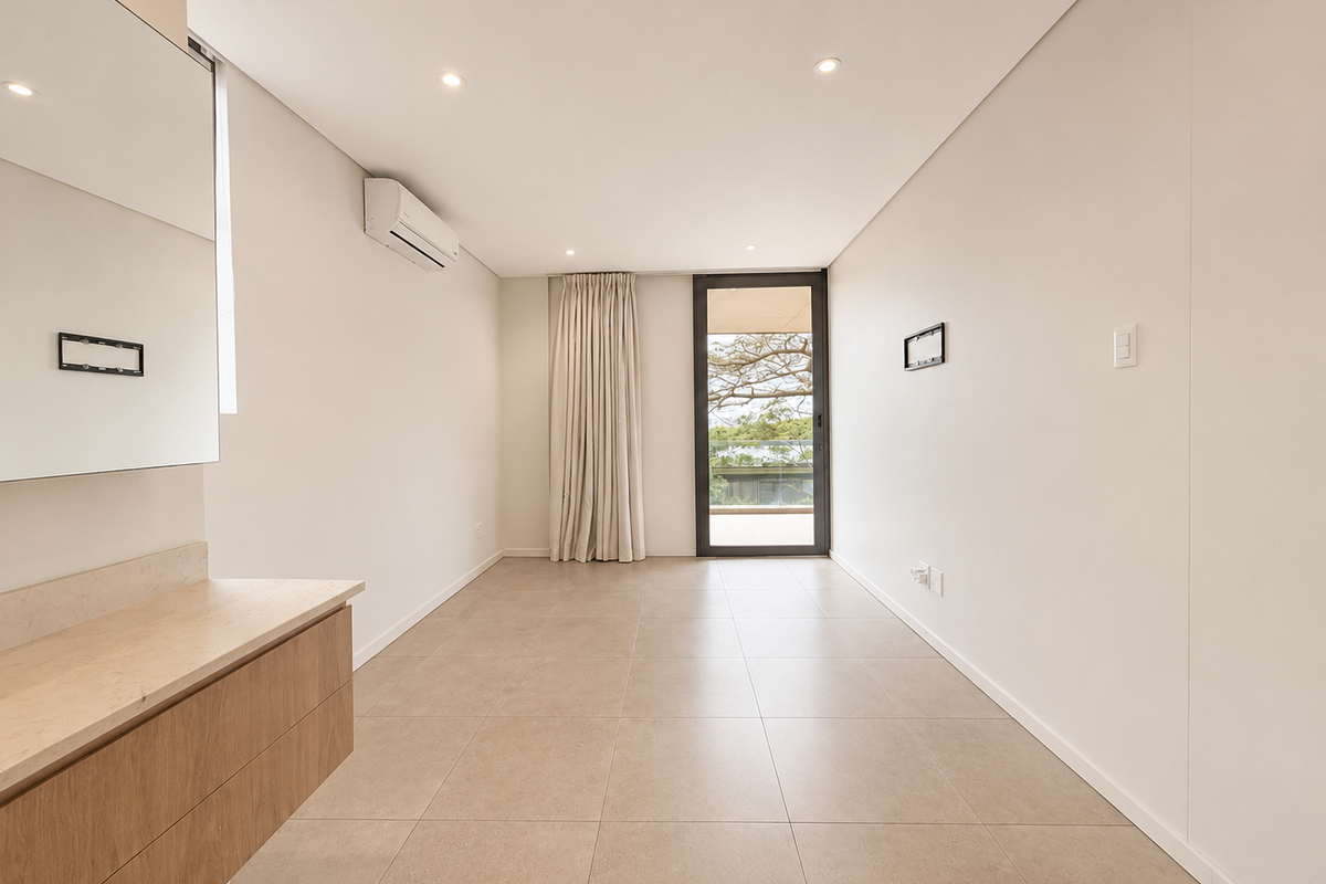 A bright, modern bedroom featuring tiled flooring, a built-in vanity unit, wall-mounted air conditioning, and direct access to a private balcony.