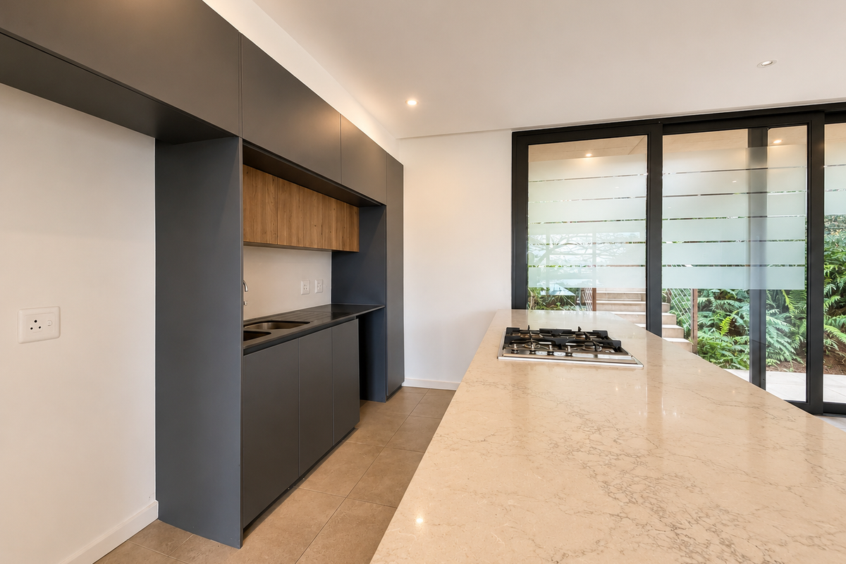 Modern kitchen featuring a large stone-topped island with an integrated gas hob, sleek dark cabinetry, and direct access to an outdoor patio area.