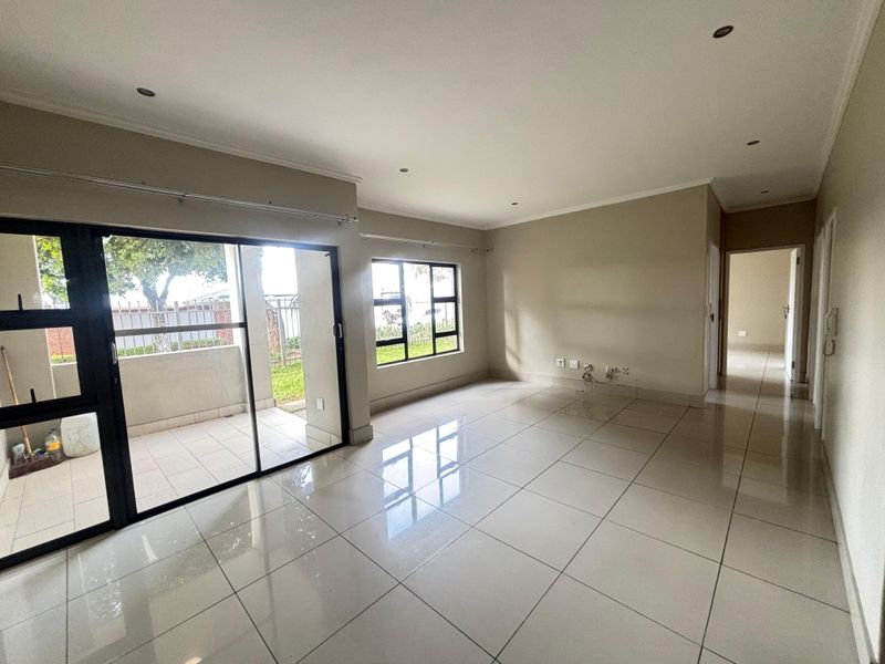 Spacious open-plan living area featuring large format floor tiles, recessed downlighting, and sliding glass doors leading to a private patio.