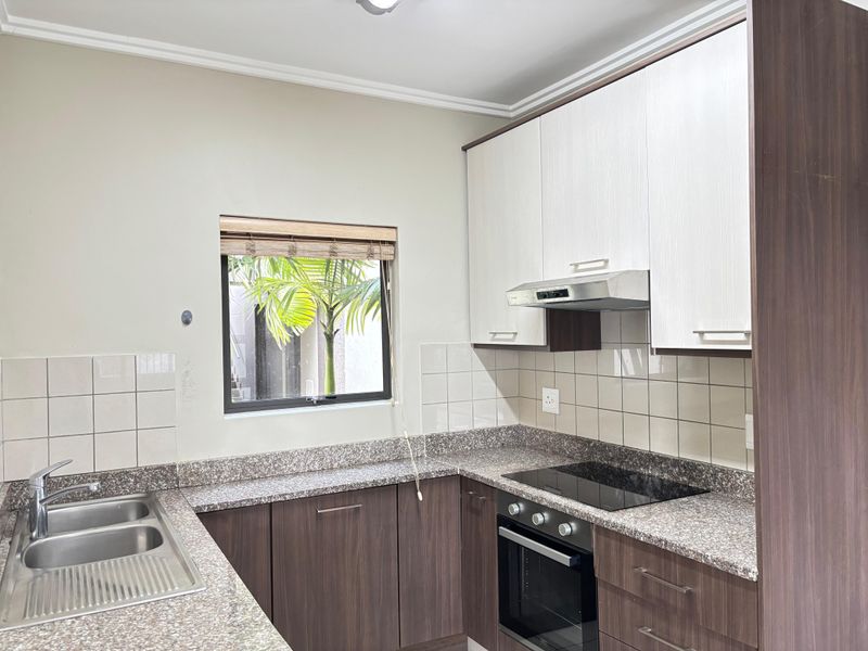 A functional kitchen featuring granite countertops, dark wood cabinetry, integrated oven, hob, and extractor fan with tiled splashbacks.