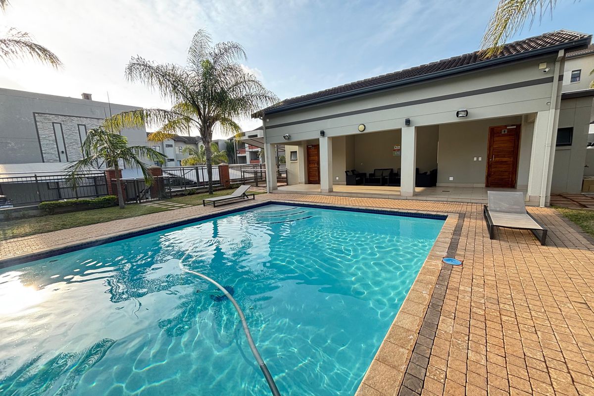 A well-maintained communal pool area featuring a paved deck, covered patio space, and landscaped surroundings within the apartment complex.