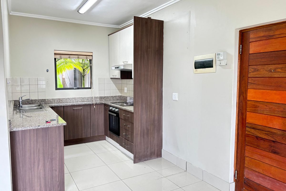 Compact kitchen featuring dark wood-look cabinetry, granite countertops, built-in oven, hob, and extractor fan, with tiled flooring and a functional layout.