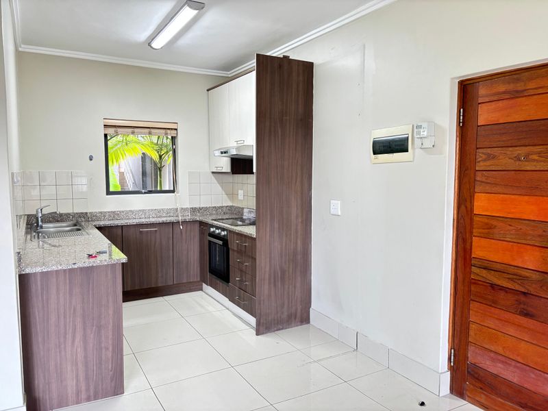 Compact kitchen featuring dark wood-look cabinetry, granite countertops, built-in oven, hob, and extractor fan, with tiled flooring and a functional layout.