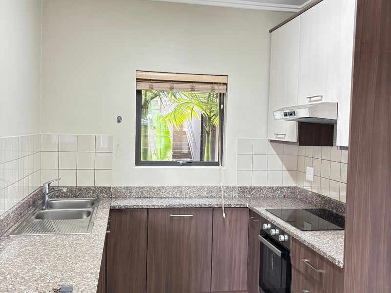 A functional kitchen featuring granite countertops, dark wood cabinetry, a built-in oven with hob, extractor fan, and a double stainless steel sink.