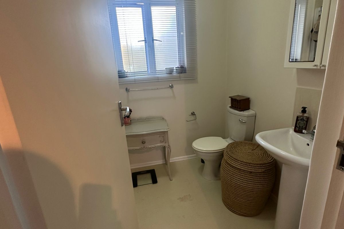 A functional bathroom featuring a pedestal sink, toilet, and a mirrored medicine cabinet, illuminated by natural light from a window with fitted blinds.