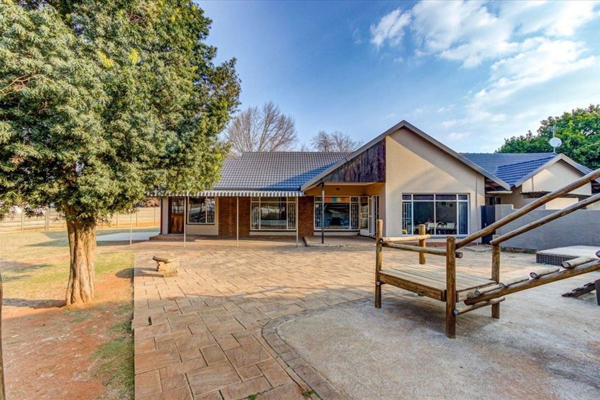 Rear view of the house featuring a spacious paved patio area, large windows, and a well-established garden setting.