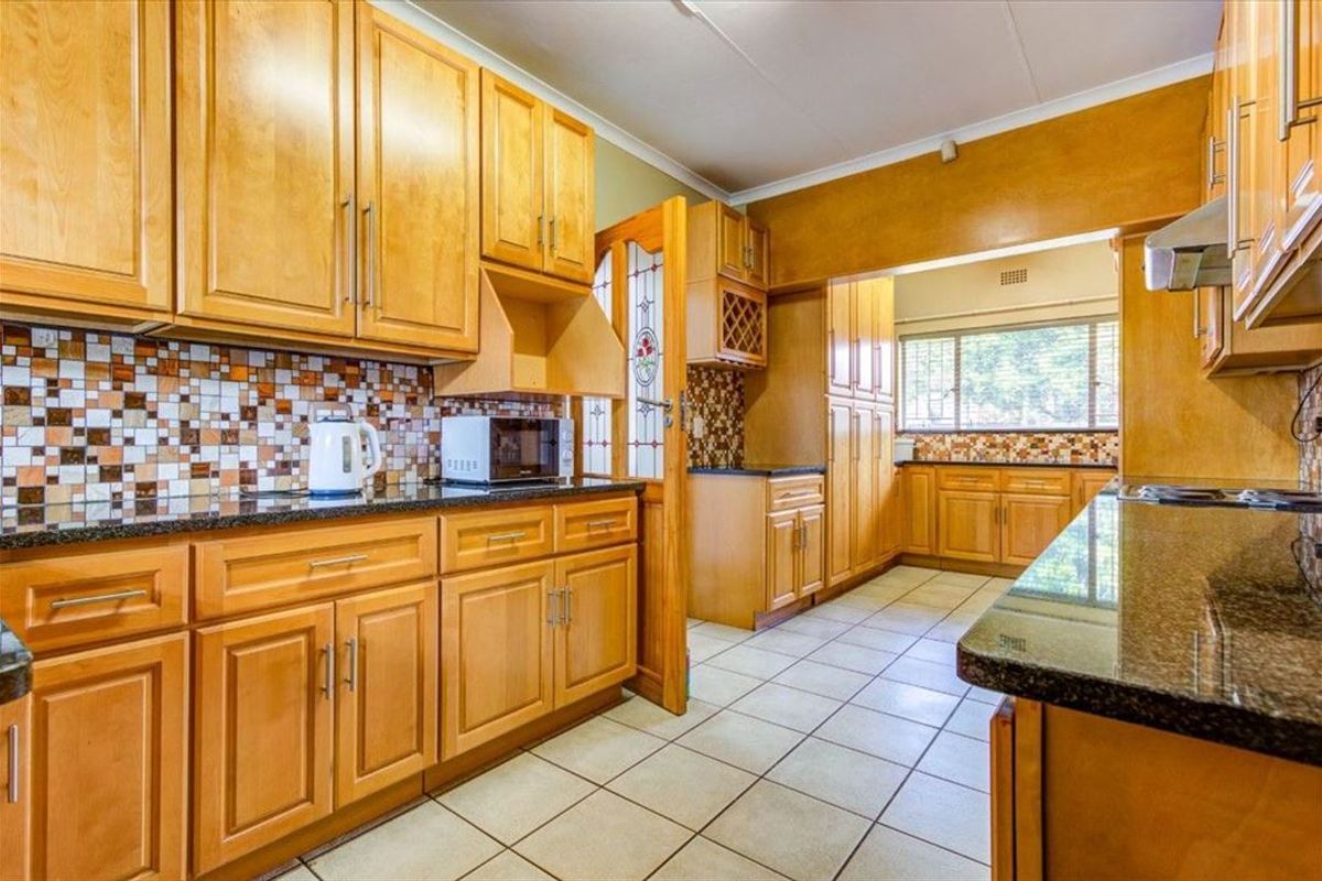 A functional kitchen featuring light wood cabinetry, granite countertops, mosaic tile backsplash, and tiled flooring with ample storage space.