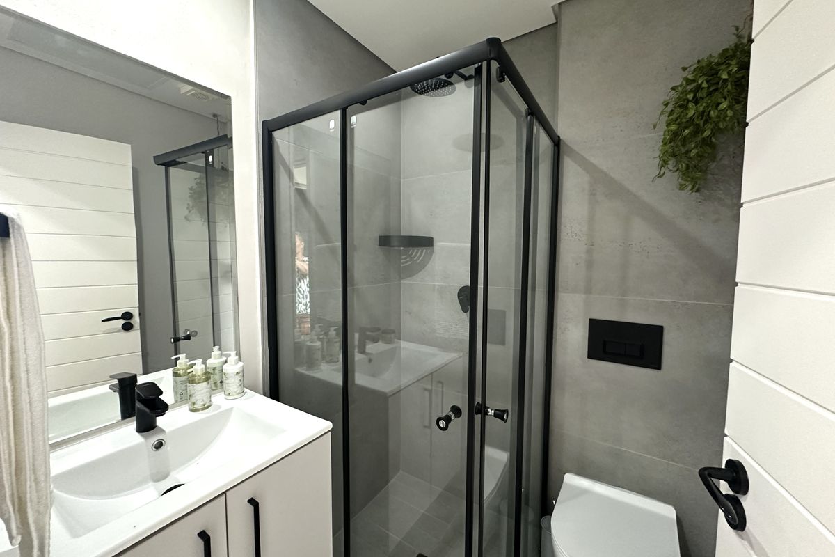 Modern bathroom featuring a glass-enclosed shower, wall-mounted toilet, and a sleek vanity with a basin and black fixtures.