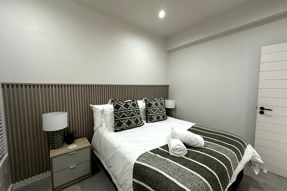 A modern bedroom featuring a decorative timber slat feature wall, recessed downlighting, and a contemporary internal door.