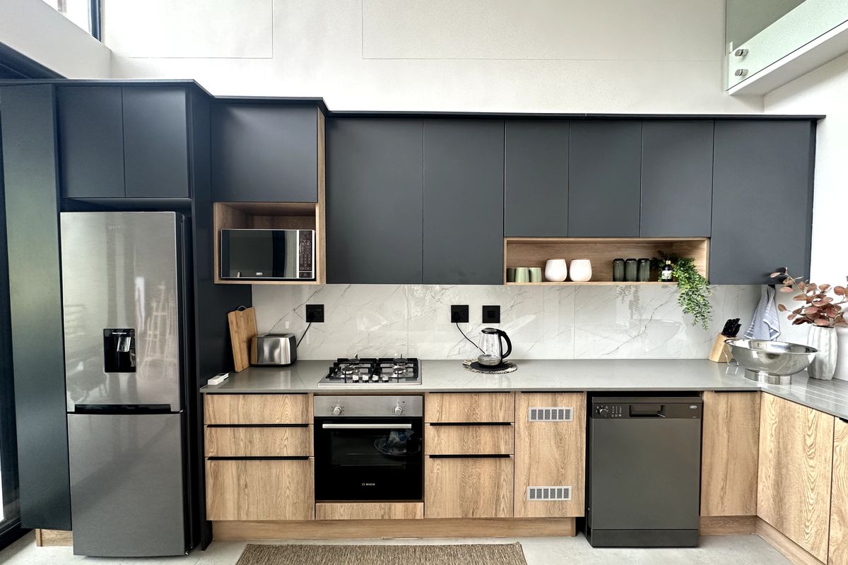 Modern kitchen featuring matte black cabinetry, wood-grain lower cupboards, stone-look backsplash, built-in oven, gas hob, and integrated dishwasher.