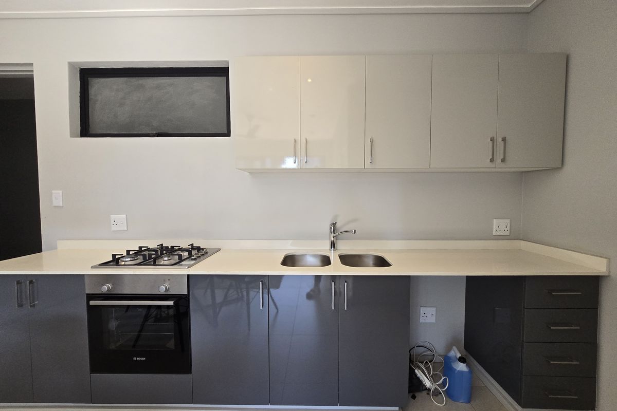 Modern kitchen featuring sleek grey and white cabinetry, stone countertops, a built-in oven, gas hob, and a double stainless steel sink.
