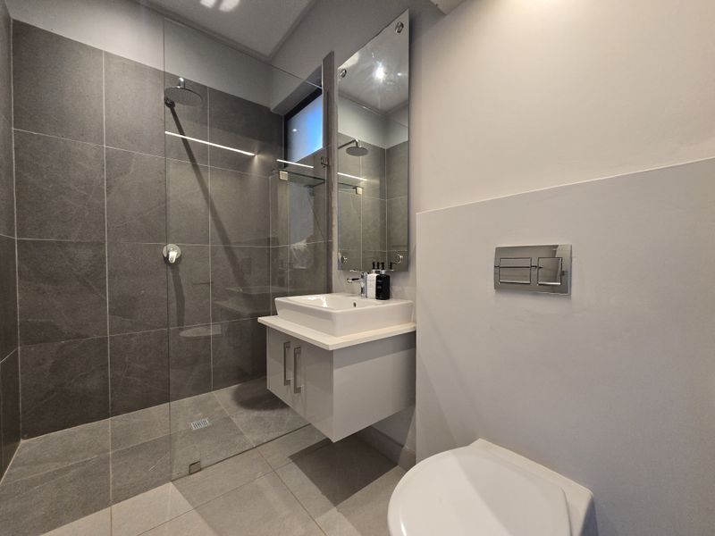 Modern bathroom featuring a walk-in shower with glass screen, wall-mounted vanity with basin, and a concealed cistern toilet with chrome flush plate.