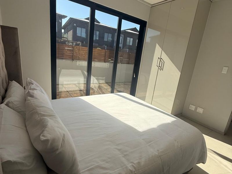 A modern bedroom featuring built-in high-gloss cabinetry, tiled flooring, recessed ceiling lighting, and large sliding glass doors leading to an outdoor area.