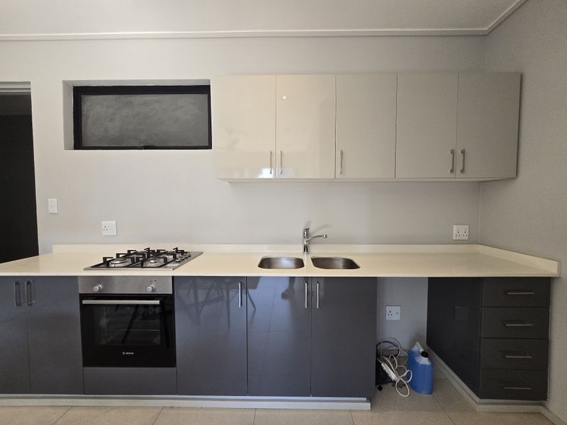 Modern kitchen featuring sleek grey and white cabinetry, stone countertops, a built-in oven, gas hob, and a double stainless steel sink.
