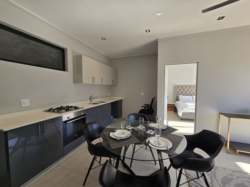 Modern open-plan kitchen featuring sleek cabinetry, integrated gas hob, and oven, seamlessly flowing into the dining area with views into the adjacent bedroom.