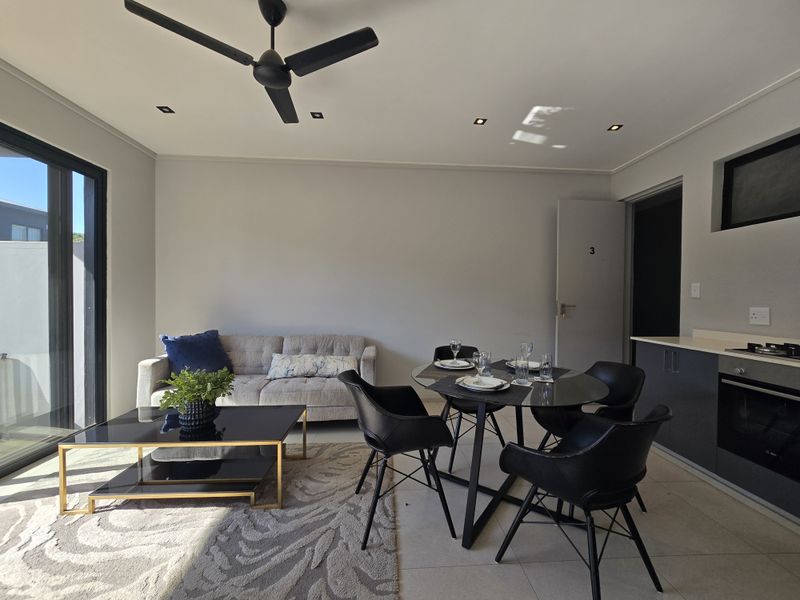 Modern open-plan living and dining area featuring a sleek kitchen, recessed lighting, ceiling fan, and large sliding glass doors leading to the outdoors.