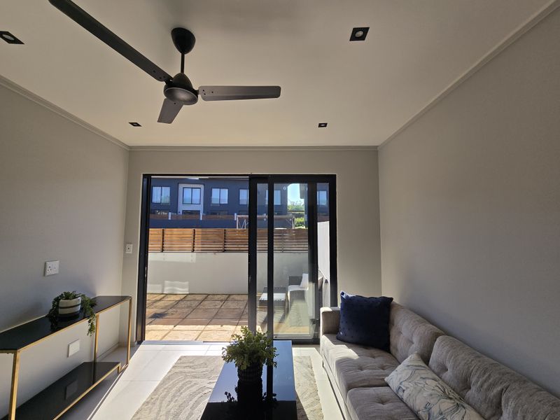 A bright living room featuring modern recessed lighting, a ceiling fan, and large sliding glass doors that open onto a private tiled patio.
