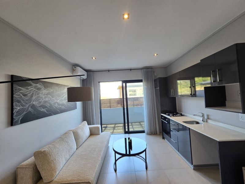 Modern open-plan living area featuring a sleek kitchen with dark cabinetry, integrated appliances, and direct access to a private balcony.