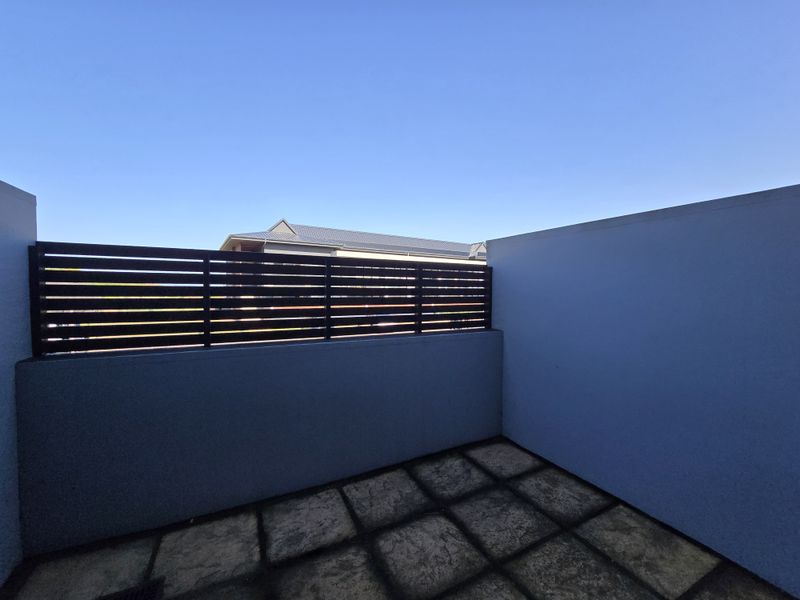 A private outdoor balcony area featuring paved flooring and a slatted privacy screen, offering a clean and functional space.