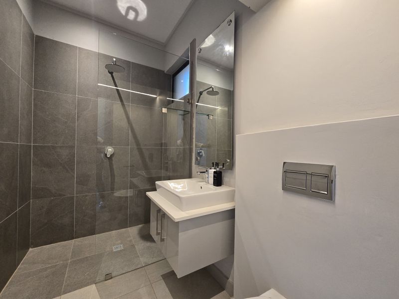 Modern bathroom featuring a walk-in shower with glass screen, wall-mounted vanity with basin, and a concealed cistern toilet.