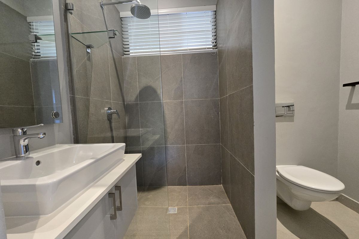 Modern bathroom featuring a walk-in shower with glass screen, wall-mounted toilet, and a sleek vanity with a countertop basin.