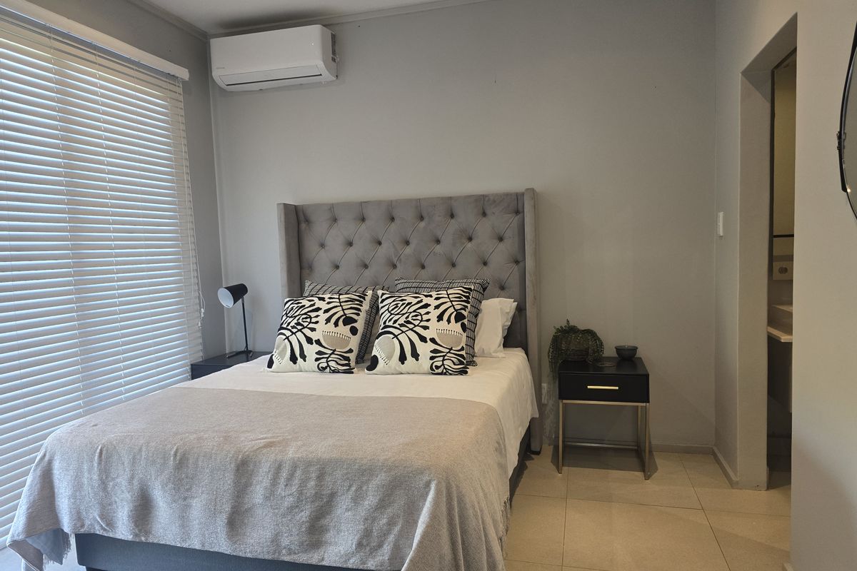 A well-maintained bedroom featuring tiled flooring, a wall-mounted air conditioning unit, and large windows with fitted blinds, offering a clean and functional living space.