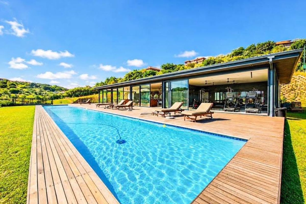 A modern outdoor pool area featuring a large swimming pool, expansive timber decking, and a seamless transition to an indoor gym space.