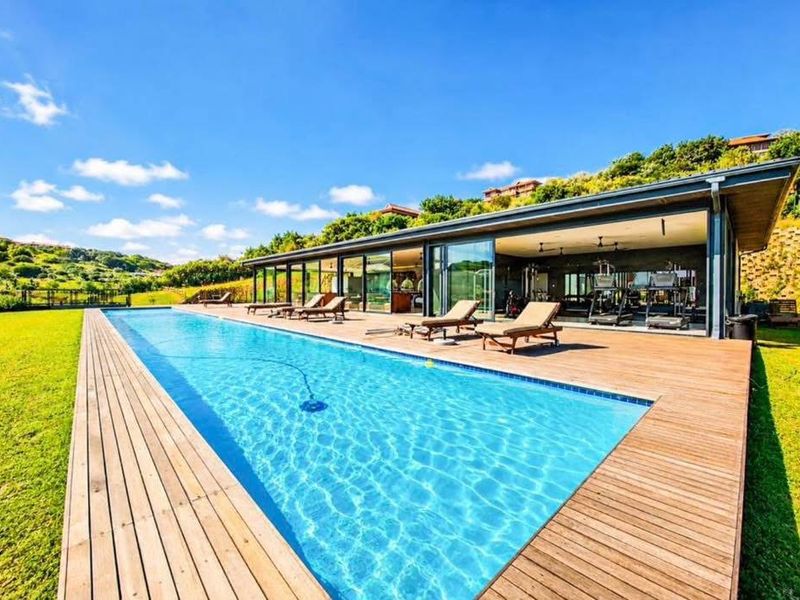 A modern outdoor pool area featuring a large swimming pool, expansive timber decking, and a seamless transition to an indoor gym space.