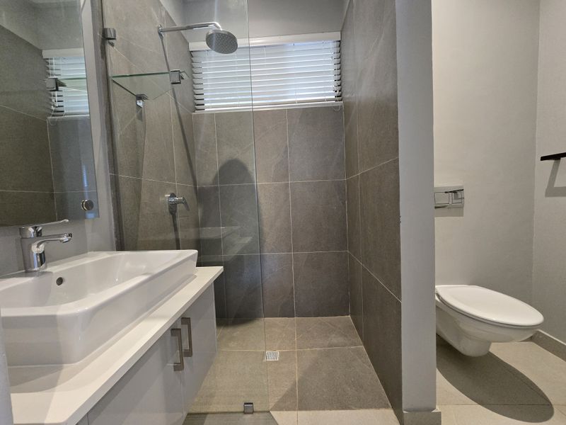 Modern bathroom featuring a walk-in shower with glass screen, wall-mounted toilet, and a sleek vanity with a countertop basin.