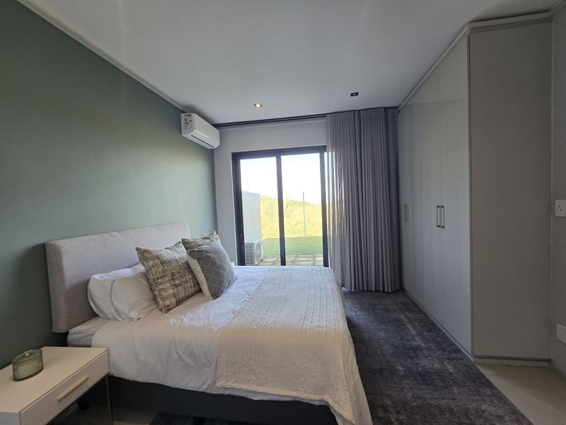 Modern bedroom featuring built-in floor-to-ceiling wardrobes, wall-mounted air conditioning unit, and sliding glass doors providing direct access to the outdoor area.