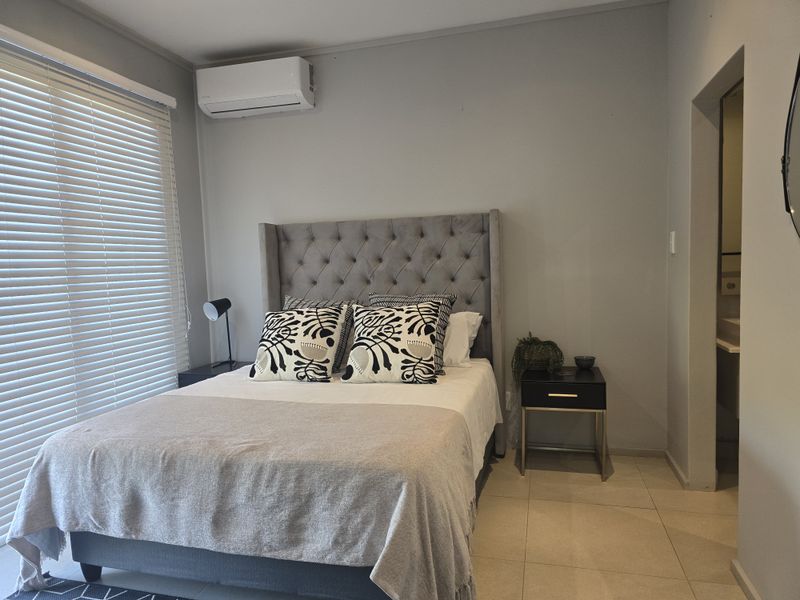A well-maintained bedroom featuring tiled flooring, a wall-mounted air conditioning unit, and large windows with fitted blinds, offering a clean and functional living space.