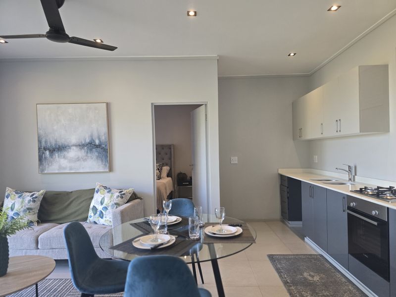 Modern open-plan living area featuring a sleek kitchen with built-in oven, hob, and cabinetry, seamlessly flowing into the dining and lounge space.