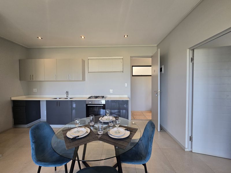 Modern open-plan kitchen featuring sleek cabinetry, built-in oven, gas hob, and tiled flooring, seamlessly flowing into the dining area.