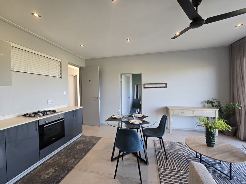 Modern open-plan living area featuring a sleek kitchen with built-in oven and gas hob, tiled flooring, and recessed ceiling lighting.