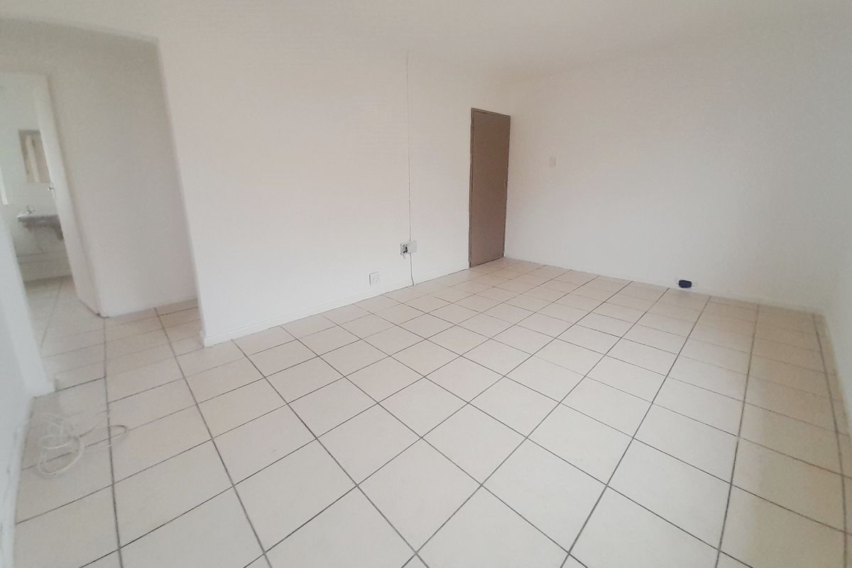 An empty living area featuring neutral ceramic floor tiles and a doorway leading to an adjacent room.